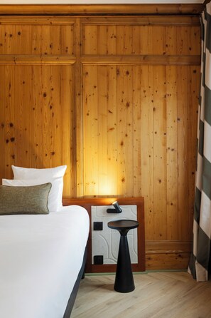 A hotel room with a wooden paneled wall, a bed with white bedding, a small table, and a nightstand. - Hôtel de l'Europe by Happyculture (Strasbourg)