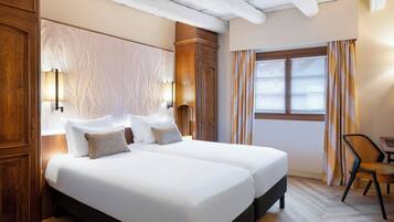 A hotel room with a large bed, two bedside lamps, a window with curtains, and a wooden chair.