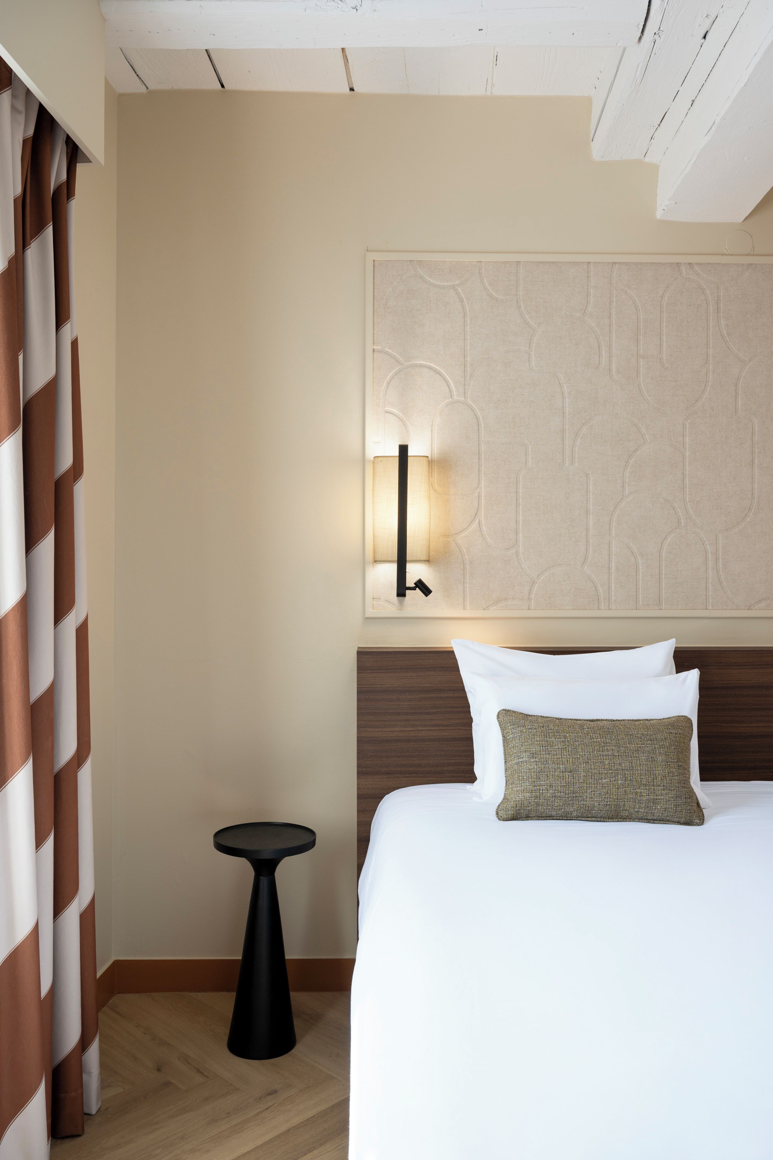 A hotel room with a bed, a nightstand, a lamp, and a patterned wall.