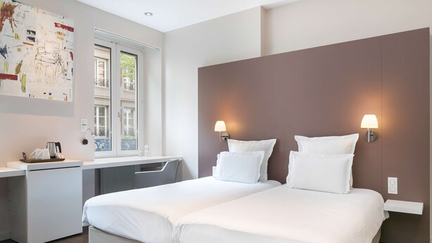 A modern hotel room with a double bed, a desk, and a window with a view of buildings. - Hôtel de l'Europe by Happyculture (Strasbourg)