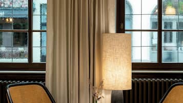 Une pièce avec deux chaises, une table, une lampe et une grande fenêtre avec des rideaux.