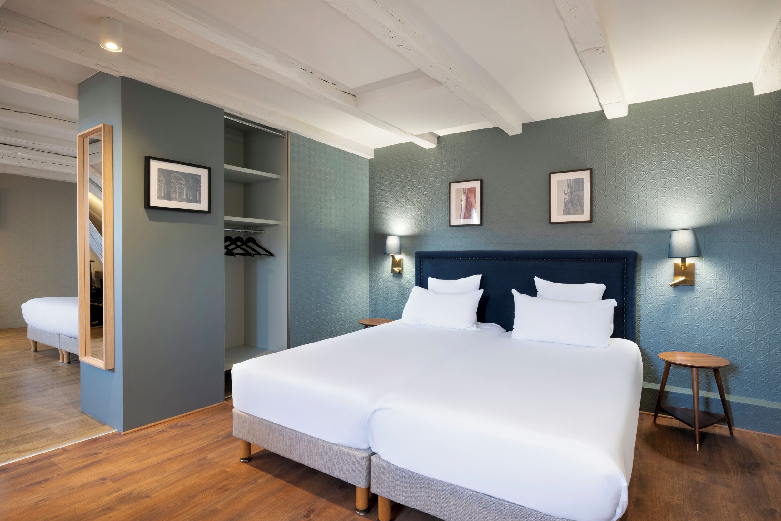 Una habitación de hotel con una cama grande, un armario, un espejo y una mesita.