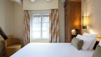 Una habitación de hotel con una cama grande, una silla, una ventana con cortinas y una lámpara fijada a la pared.