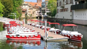 A marina with red boats docked, a bridge, and buildings in the background. - Hôtel de l'Europe by Happyculture (Strasbourg)