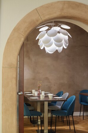 Un comedor con una mesa preparada para cuatro personas, rodeado de sillas azules, bajo una lámpara esférica original.