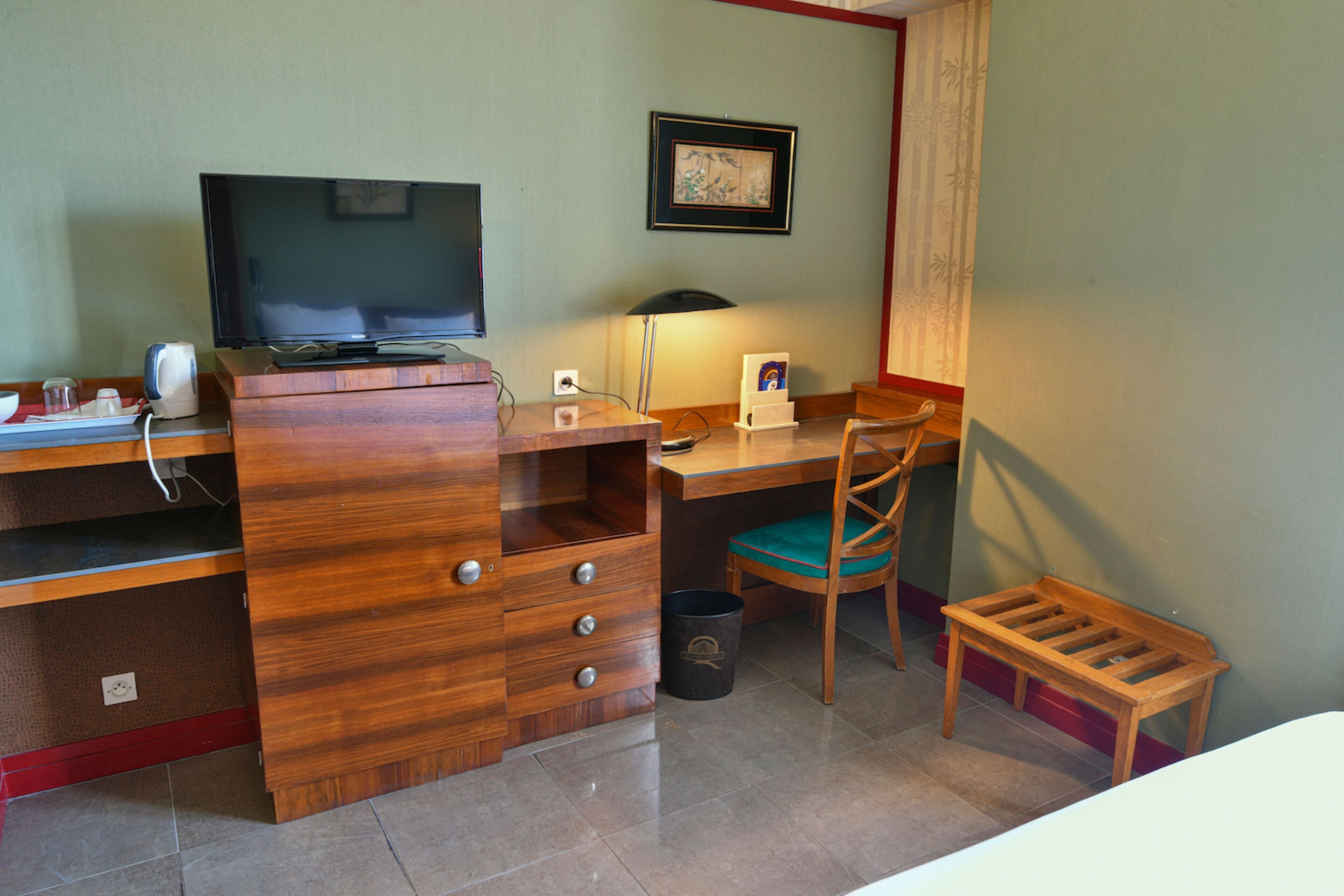 Ein Hotelzimmer mit einem Holztisch, einem Fernseher, einer Lampe, einem Sessel, einem kleinen Tisch und einem Mülleimer.
