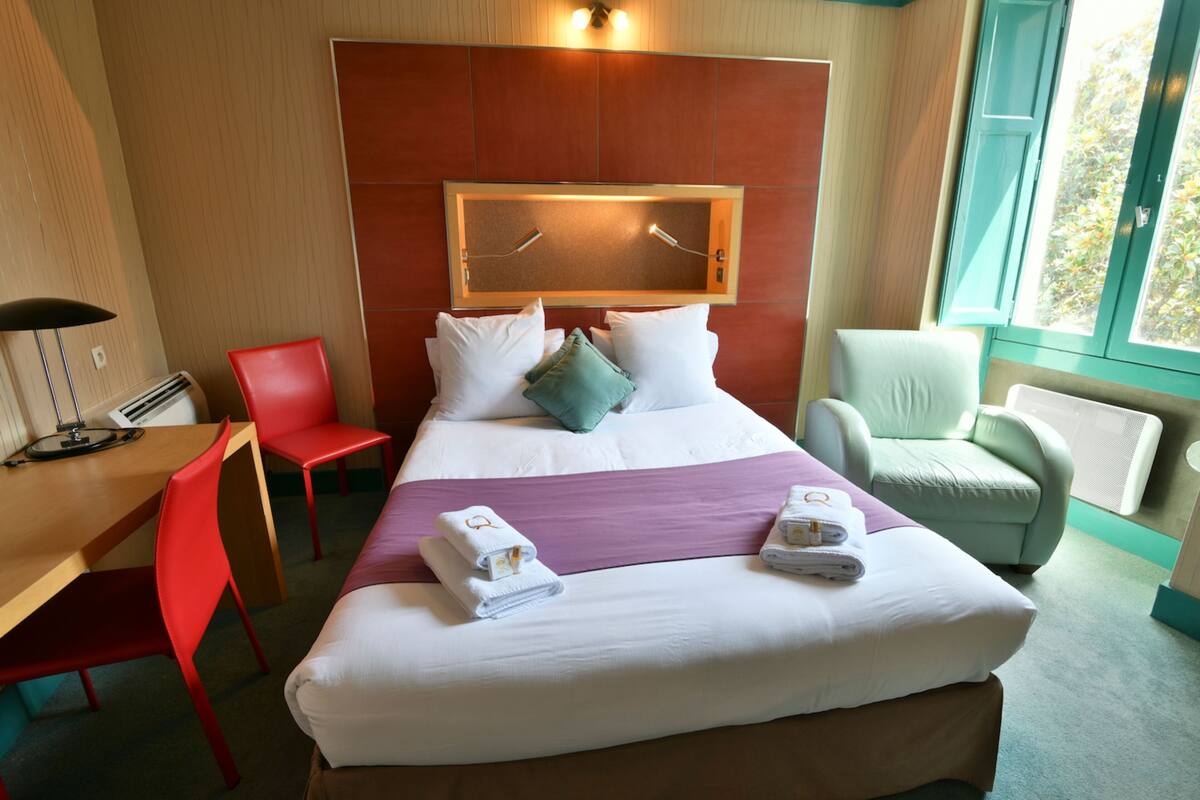 A hotel room with a large bed, two chairs, a desk, and a window.