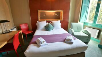 Een hotelkamer met een groot bed, twee stoelen, een bureau en een raam.
