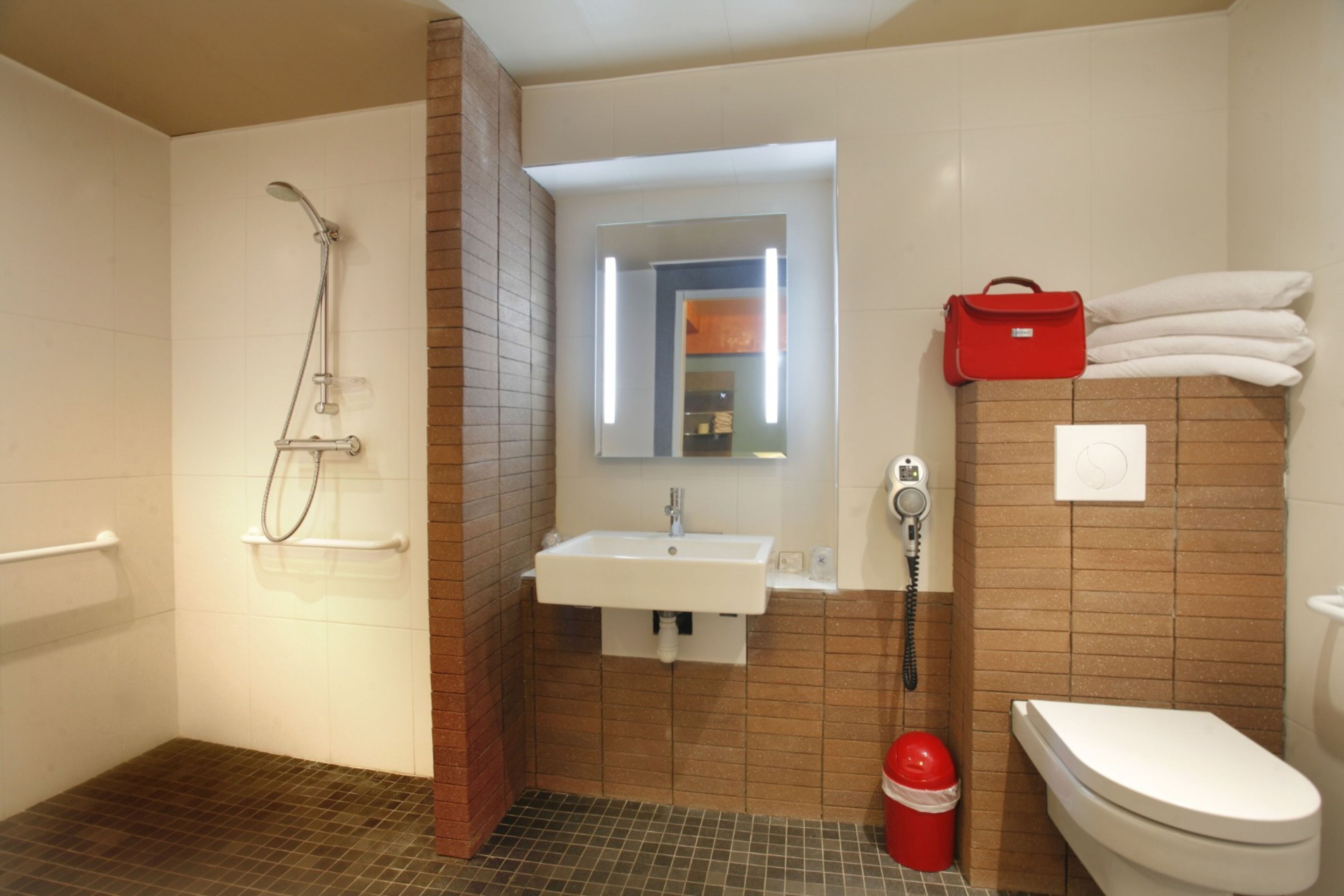 Ein Badezimmer mit Dusche, Waschbecken, Toilette und einer roten Tasche, die an der Wand hängt.