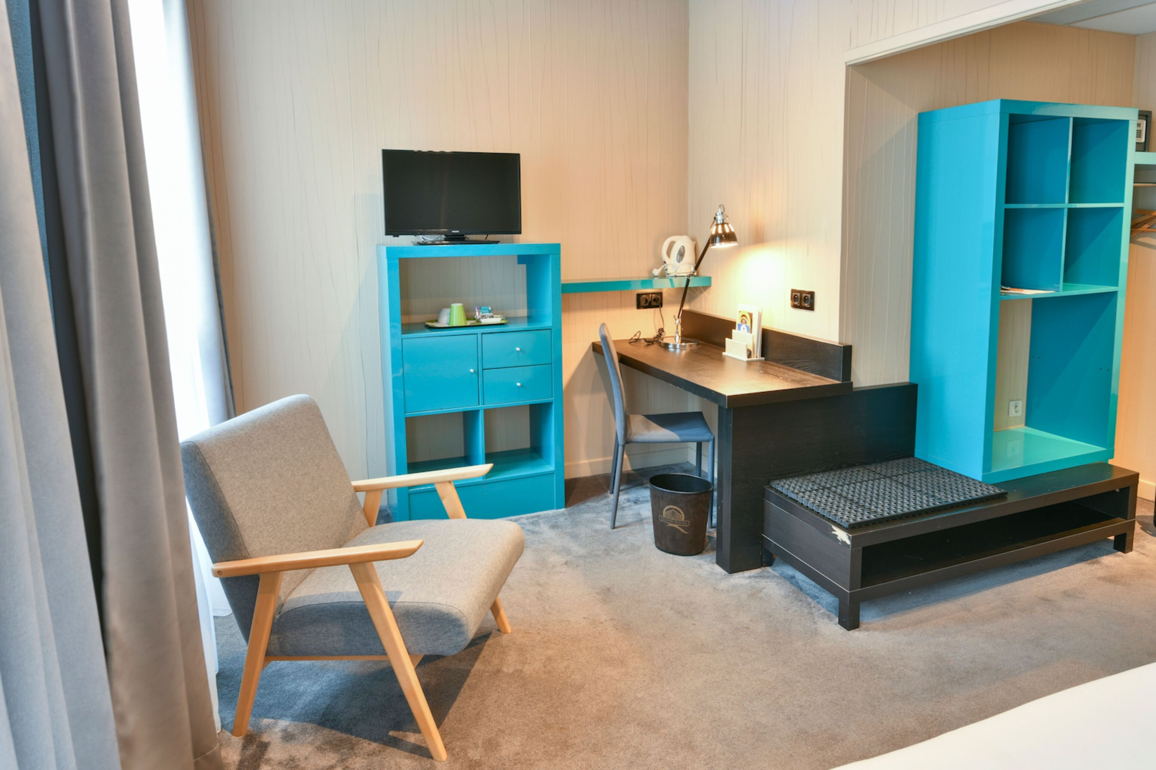 A hotel room with a desk, chair, television, and a large blue wardrobe.