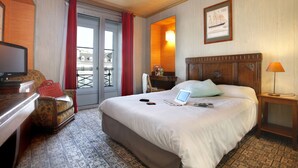 Una camera d'albergo con un letto, una scrivania con un portatile, una sedia, una televisione e una finestra con tende.