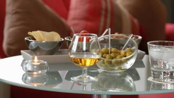 A table with a glass of amber liquid, a bowl of olives, a small bowl of chips, and a glass of water.
