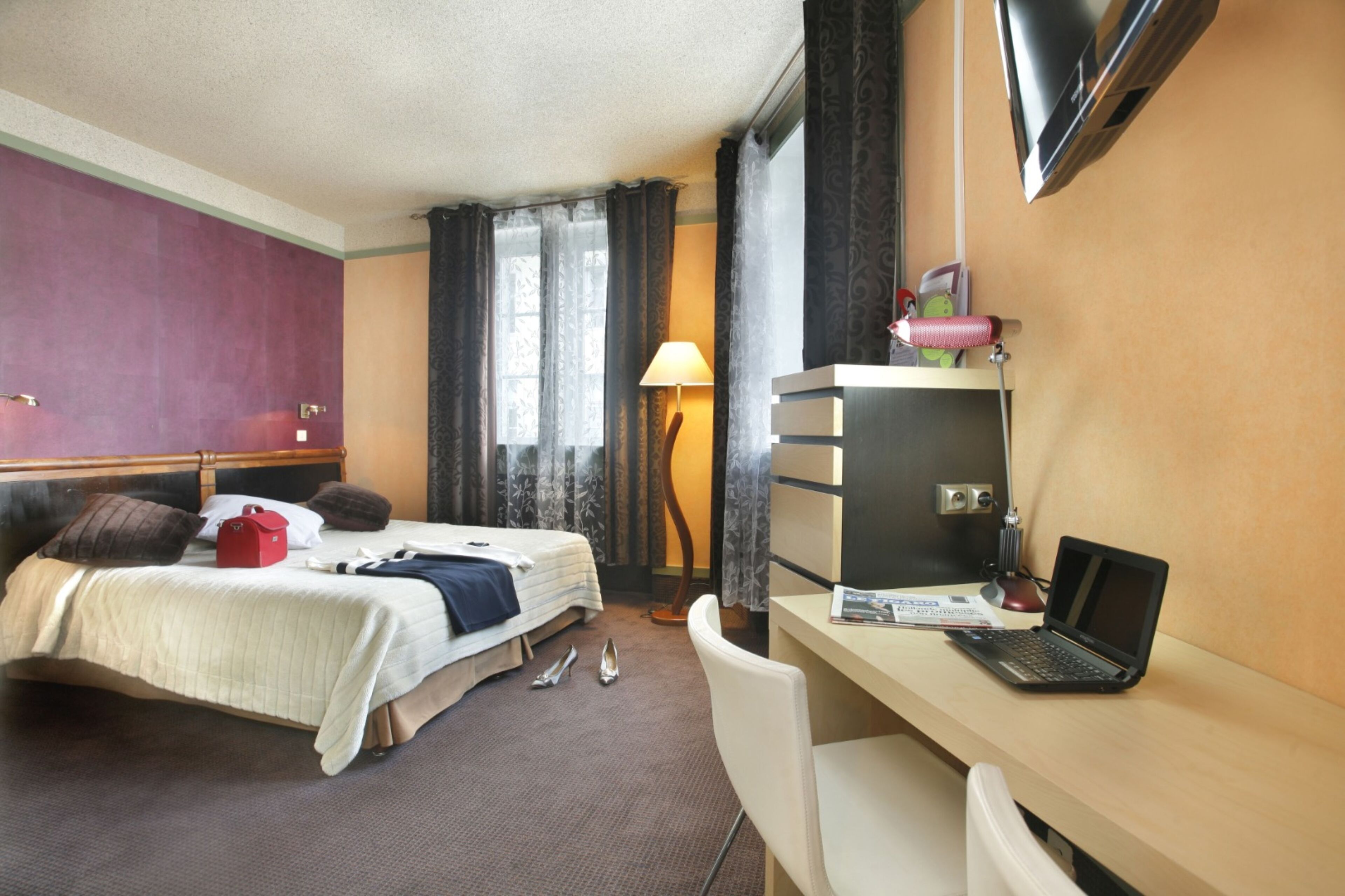 A hotel room with a bed, desk, chair, and a TV mounted on the wall.