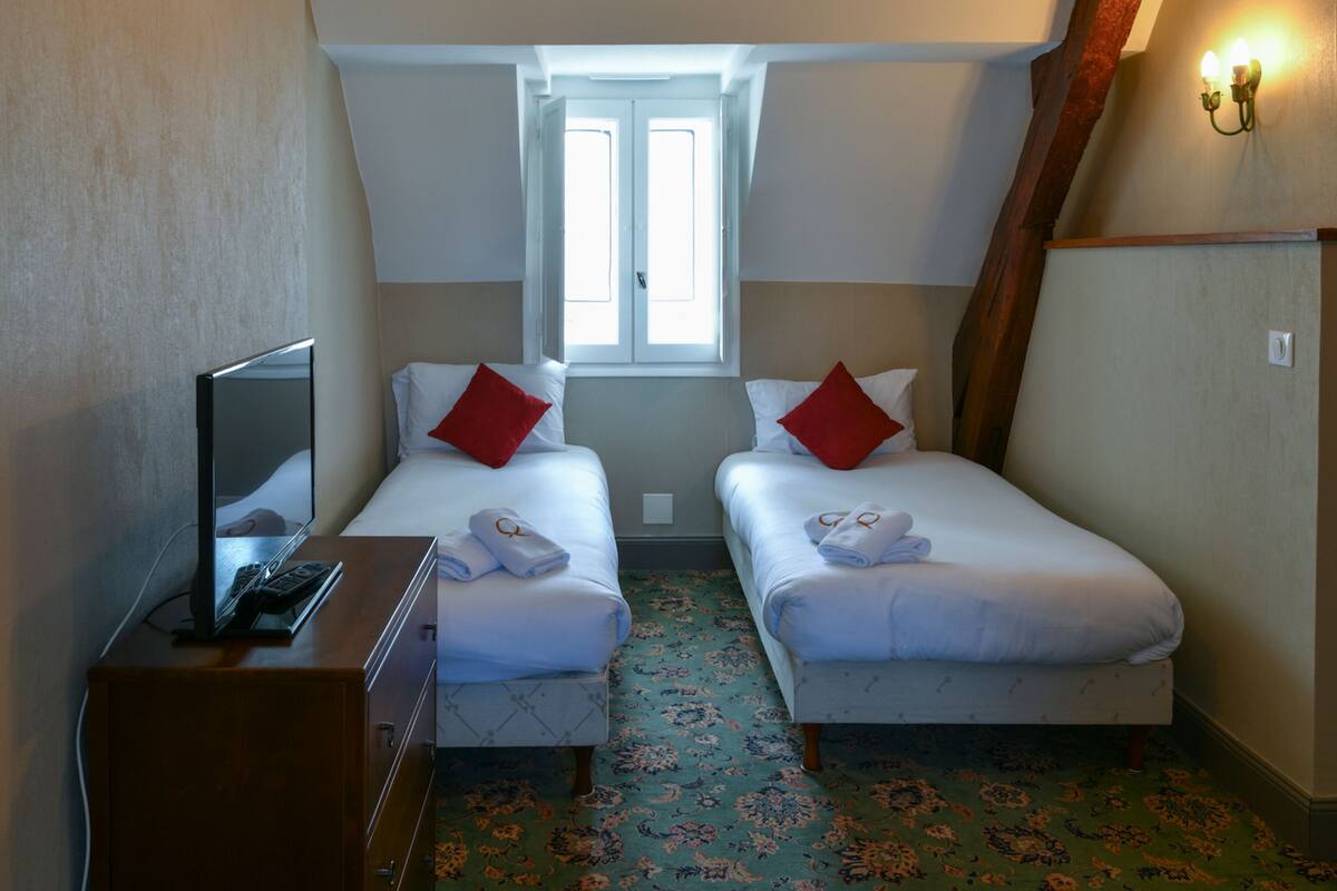 A hotel room with two beds, a desk with a computer, a window, and a patterned carpet.