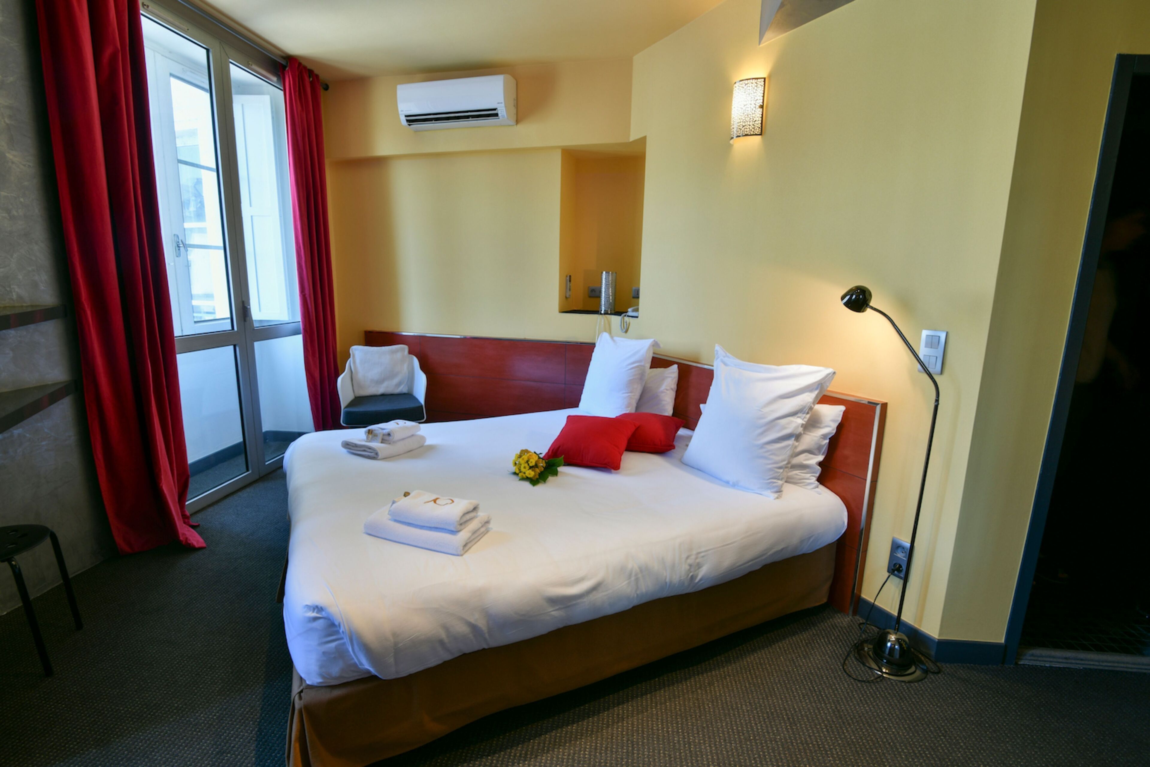 Une chambre d’hôtel avec un grand lit, des rideaux rouges, un climatiseur, une table de chevet et une lampe.
