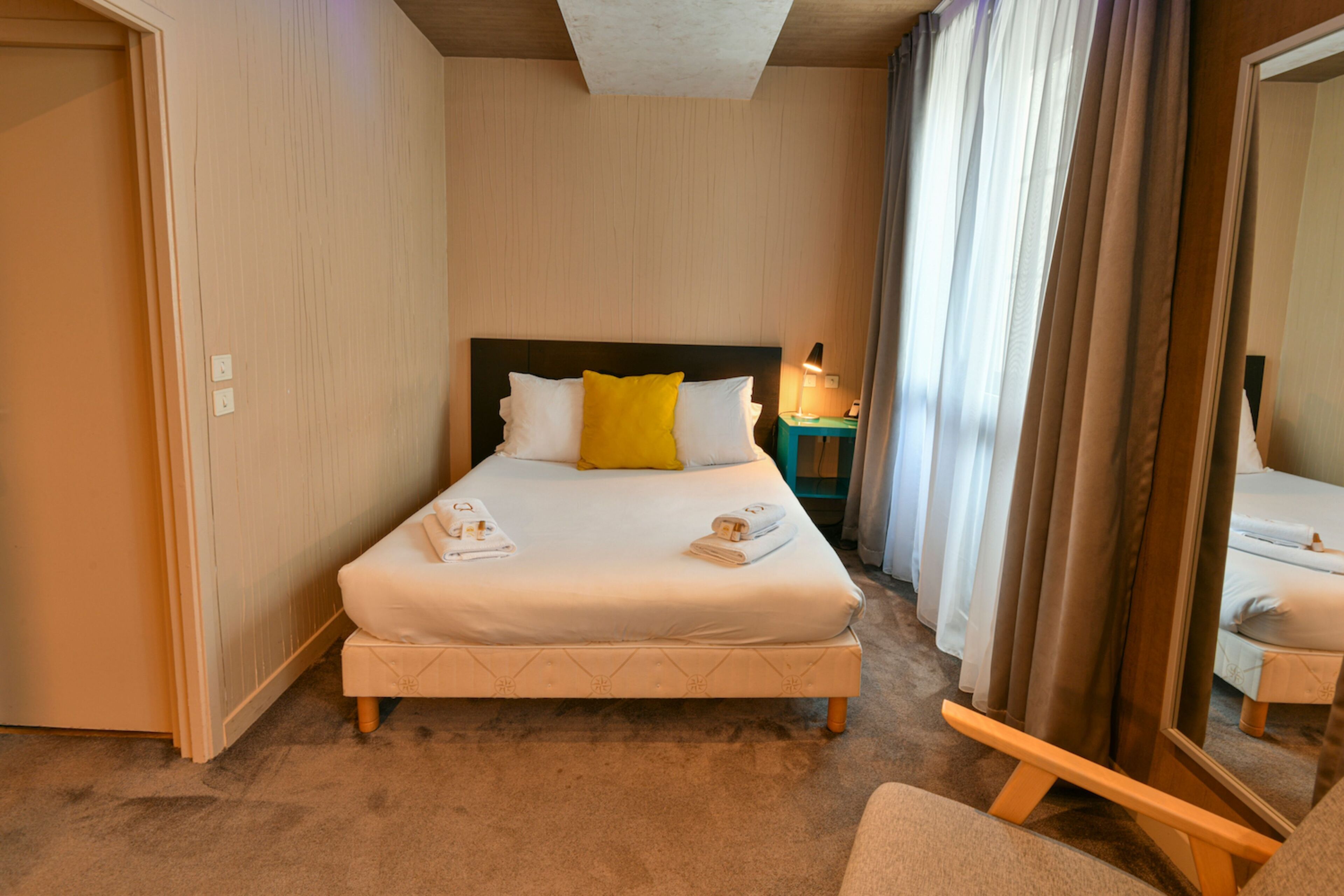 A hotel room with a bed, a nightstand, a mirror, and a door.