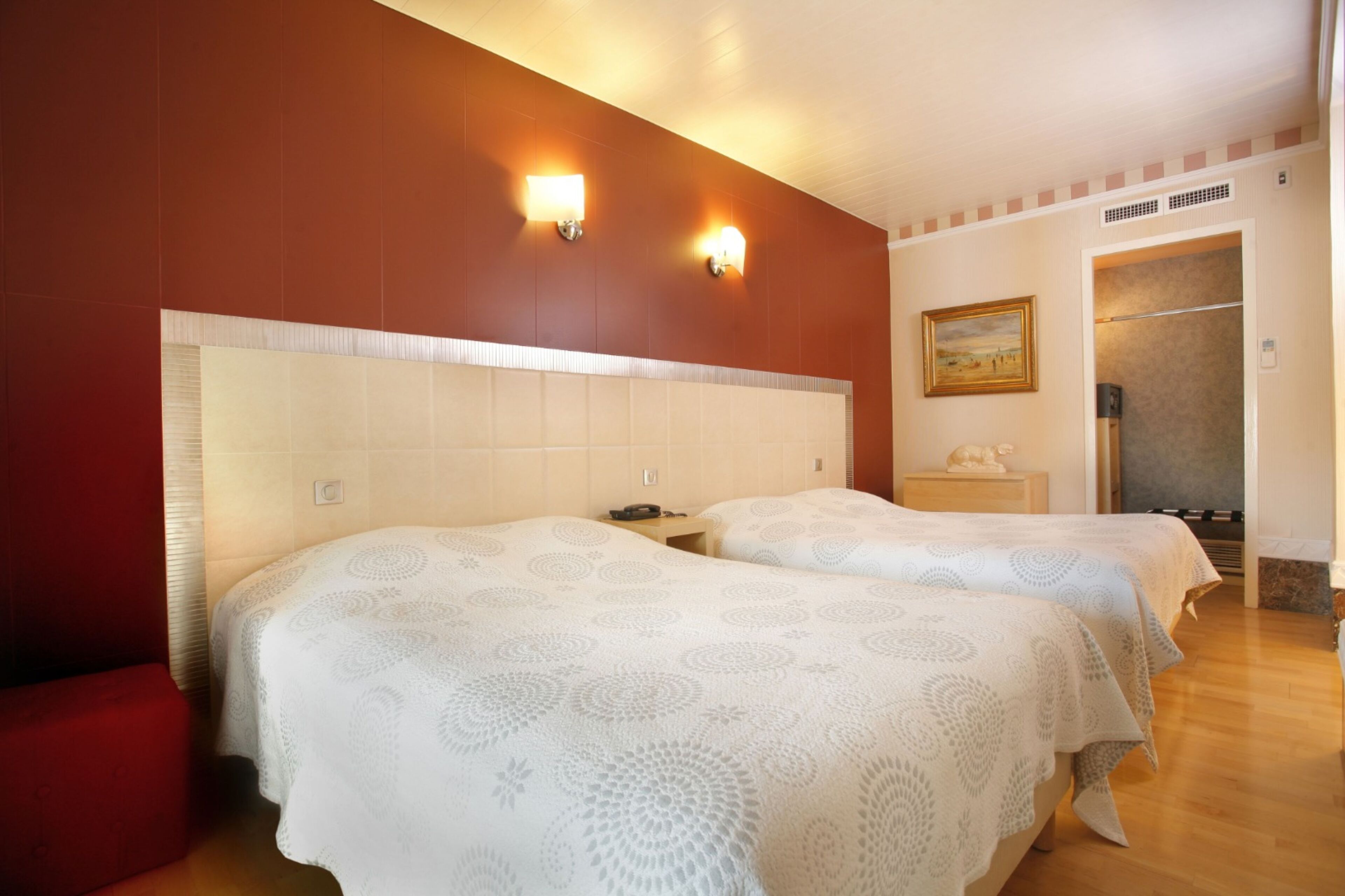 A hotel room with two beds, a red wall, and a painting on the wall.