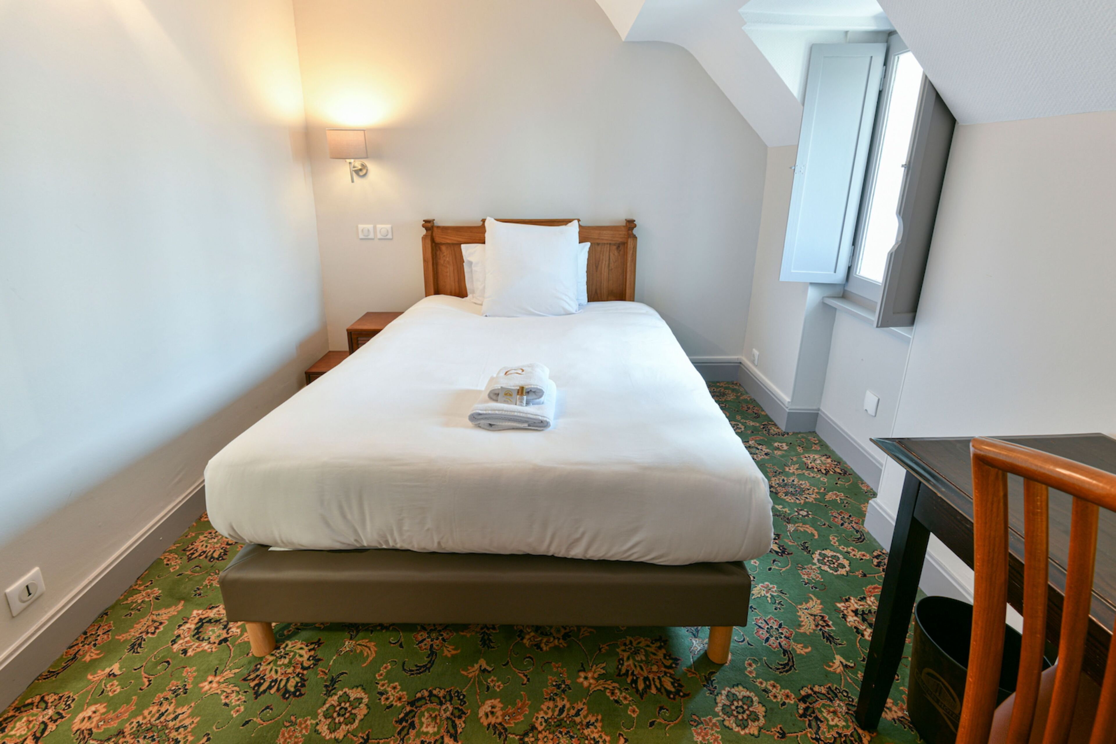A neatly made bed with a wooden headboard, a bedside table, and a wall-mounted light.