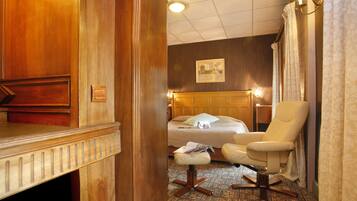 A hotel room with a wooden dresser, a bed with a headboard, a chair, and a patterned carpet.