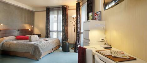 Ein Hotelzimmer mit einem Bett, einem Schreibtisch, einem Stuhl, einem Koffer und einem Fenster mit Vorhängen.
