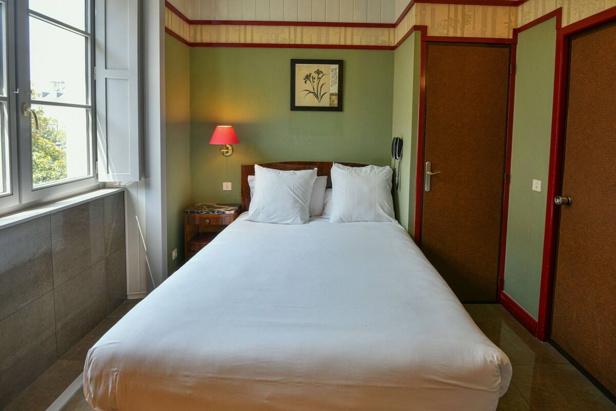 A hotel room with a bed, a nightstand, a lamp, a framed picture on the wall, and a door.