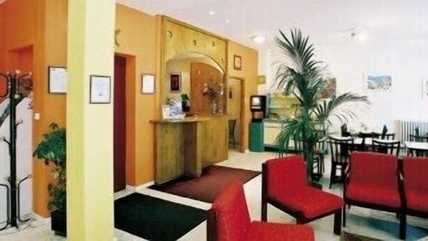 Un hall d’hôtel avec un comptoir d’accueil, des sièges rouges et un escalier.