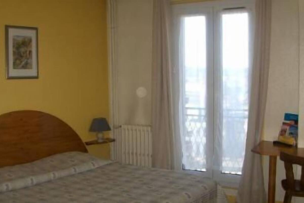 A bedroom with a bed, a nightstand, a lamp, and a window with curtains.
