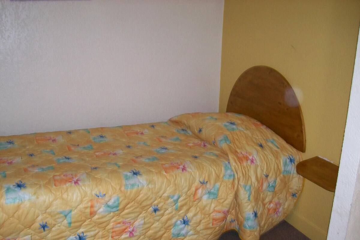 A small, single-bed room with a wooden headboard and a floral-patterned bedspread.