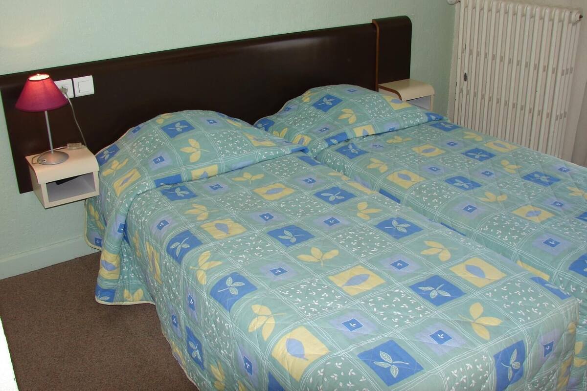 A double bed with a floral patterned bedspread, a bedside table with a lamp, and a radiator on the wall.