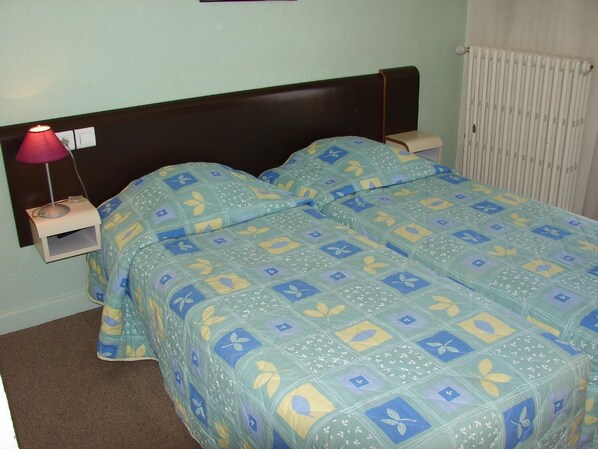 Un lit double avec une couvre-lit à motifs floraux, une table de chevet avec une lampe et un radiateur fixé au mur.