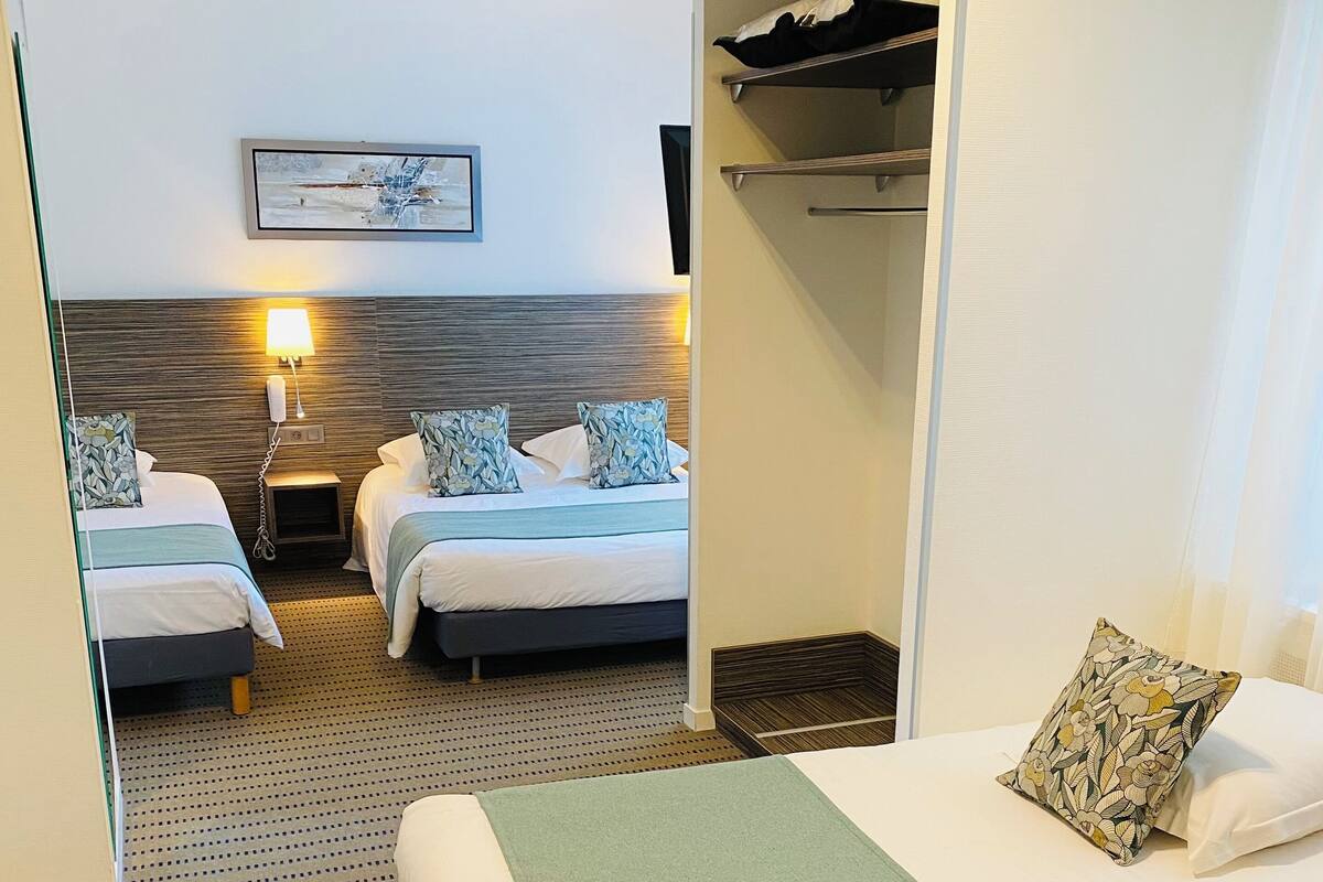 Une chambre d’hôtel avec deux lits, une couverture verte, un oreiller à motifs, une table de chevet avec une lampe et un tableau encadré au mur.