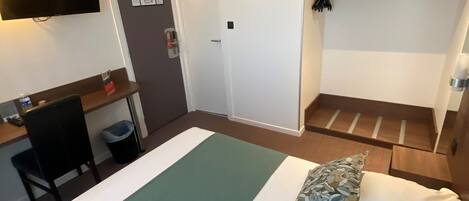 Habitación de hotel con cama, escritorio, silla, televisor y puerta.