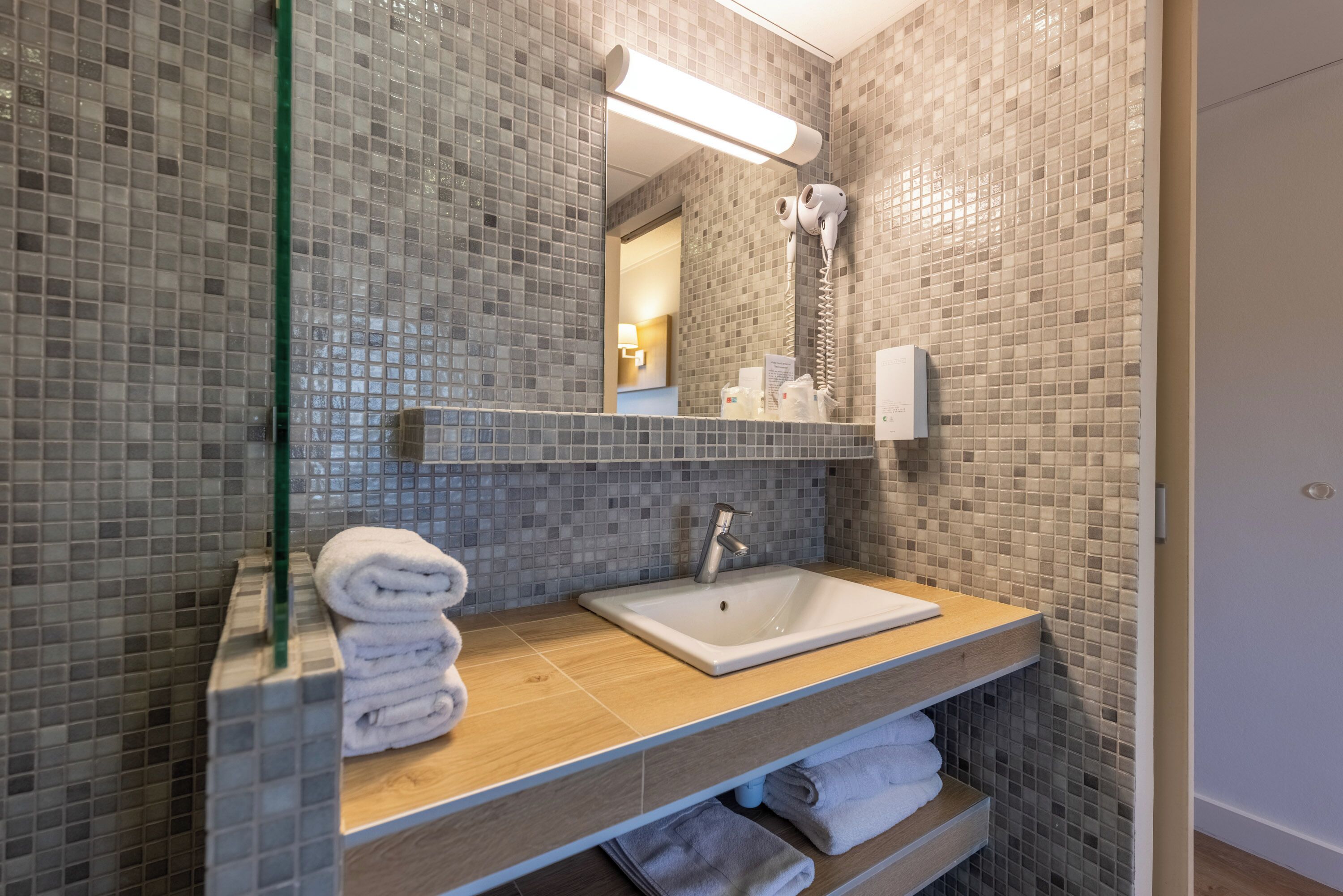 A bathroom with a tiled backsplash, a sink, a mirror, a towel rack, and a handheld showerhead.