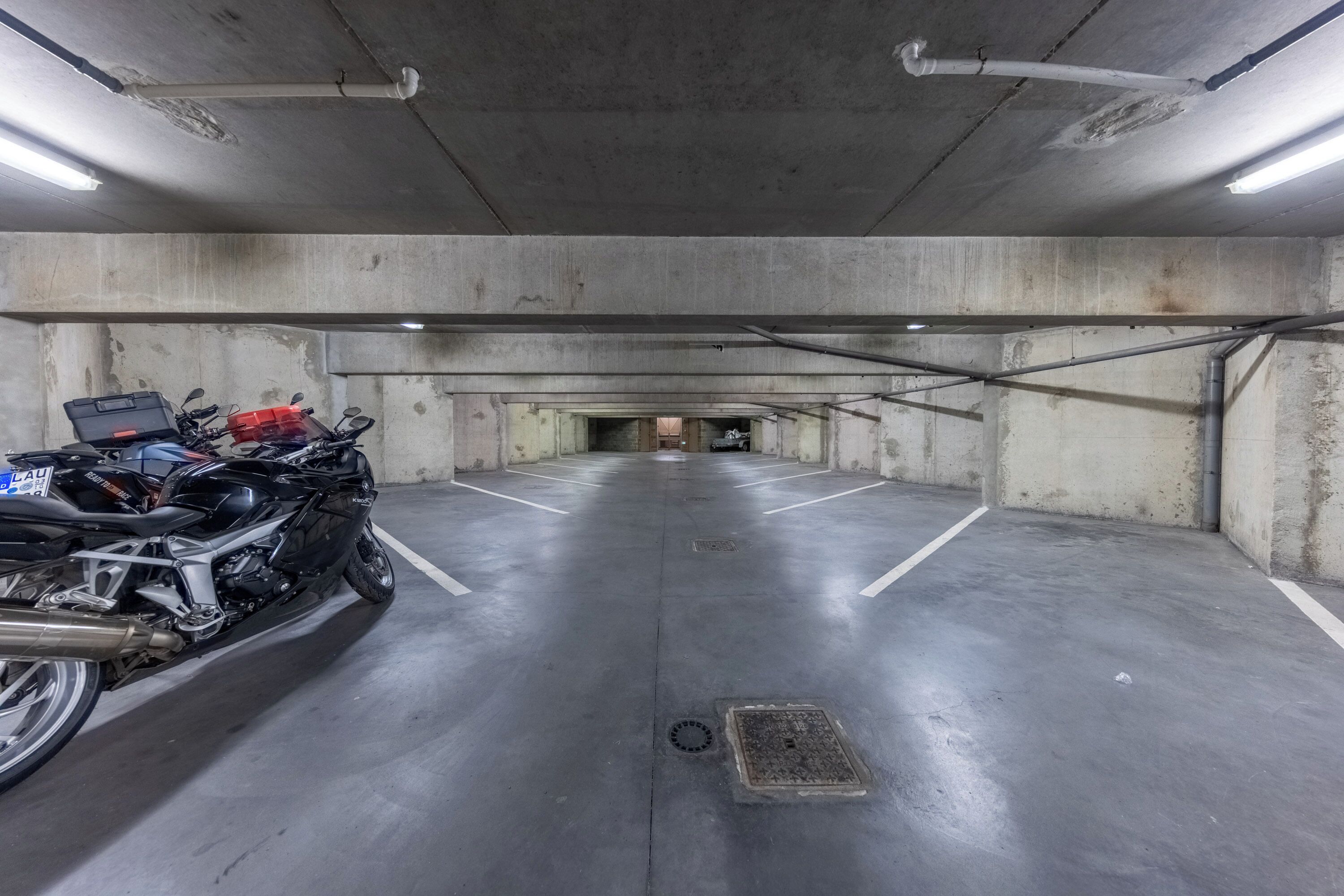Um estacionamento com paredes de concreto e uma motocicleta estacionada em primeiro plano.
