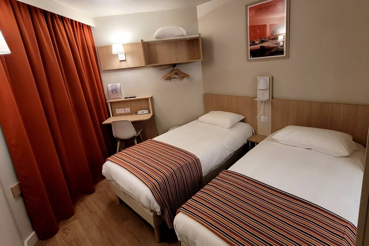 Habitación de hotel con dos camas, un escritorio, una silla, una lámpara y un cuadro en la pared.