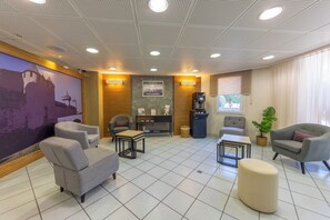A modern lounge area with grey sofas, a coffee machine, and a large wall mural. - Hotel Espace Cité (Carcassonne)