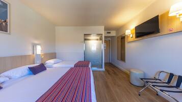 Una habitación de hotel con una cama, lámparas de noche, un televisor montado en la pared y una silla.