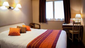 Habitación de hotel con una cama grande, dos almohadas, un escritorio con silla y una ventana con cortinas.