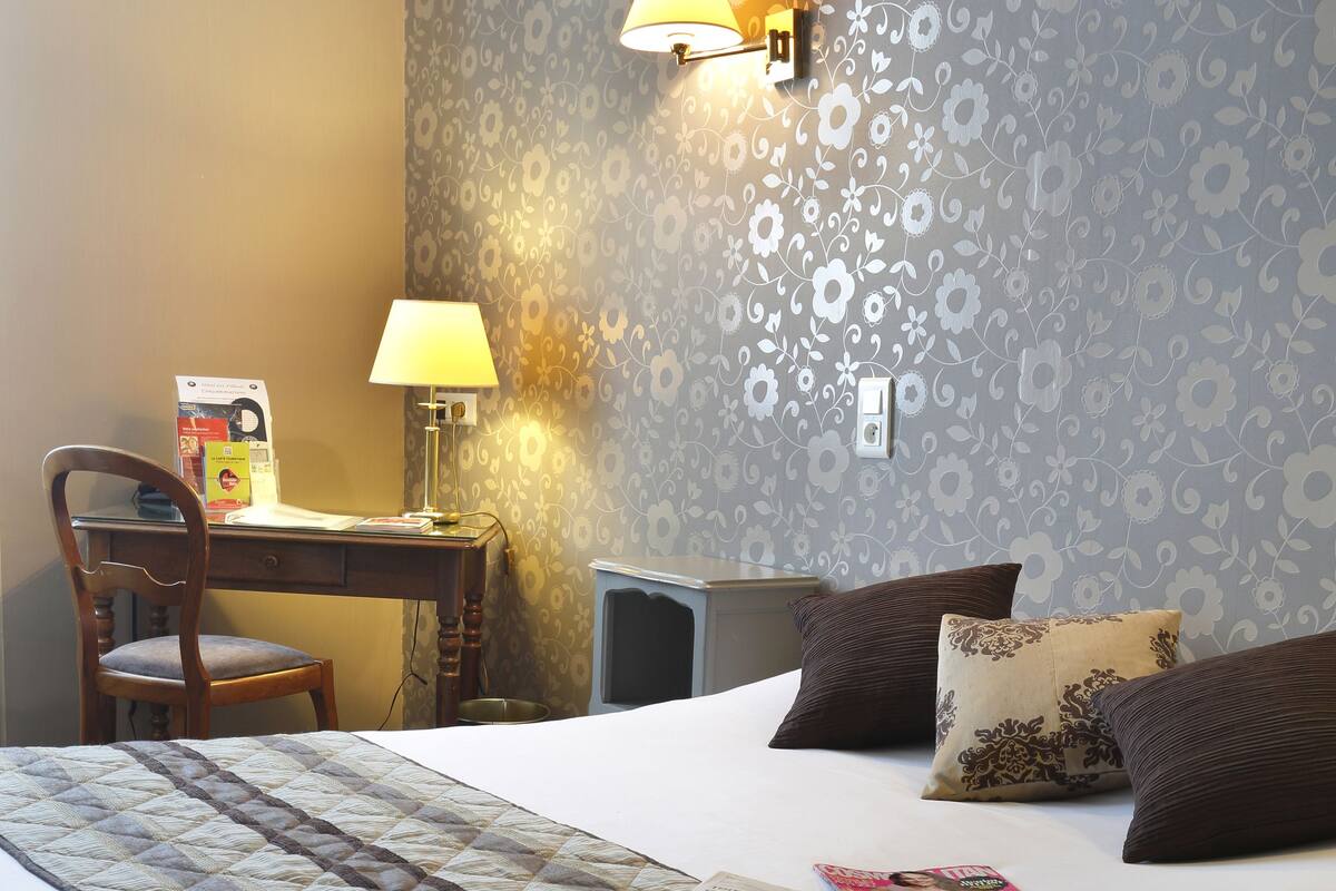 A neatly made bed with a quilt, a desk with a lamp, and a chair in a hotel room.