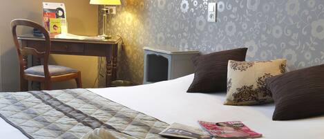 A neatly made bed with a quilt, a desk with a lamp, and a chair in a hotel room.
