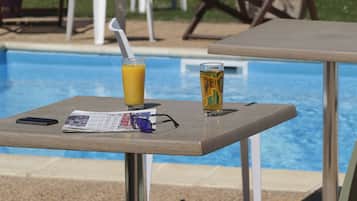 A poolside table with a drink, sunglasses, and a newspaper.