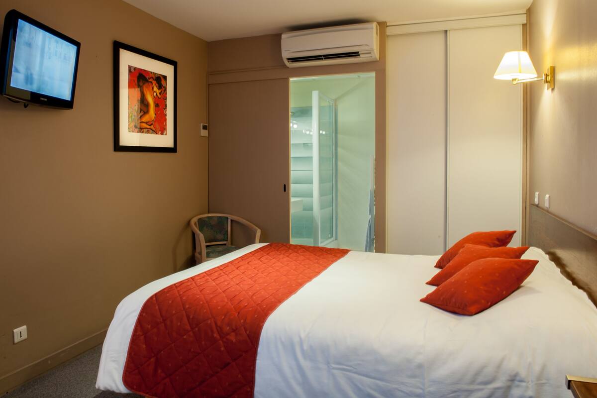 A hotel room with a bed, a television, an air conditioner, and a framed picture on the wall.