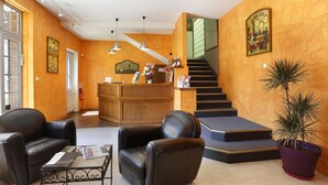 A lobby with a reception desk, two leather chairs, a coffee table, a staircase, and a potted plant. - Hôtel Les Tilleuls, Bourges (Bourges)