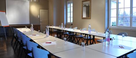 Un salón de conferencias con una larga mesa, sillas, una pantalla de proyector y ventanas.