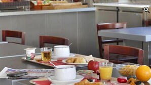 A breakfast setting with a table set for two, including plates of food, a beverage, and a newspaper. - Hôtel Les Tilleuls, Bourges (Bourges)