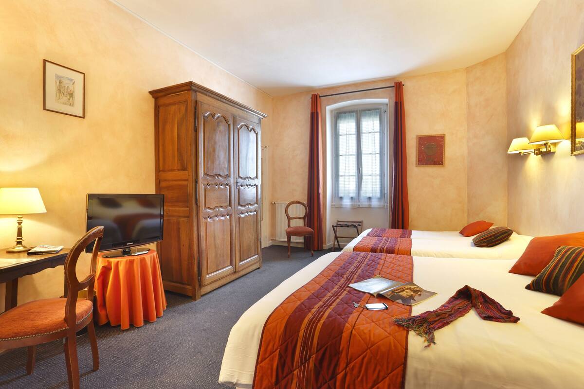 A hotel room with two beds, a television, a desk with a lamp, and a wardrobe.