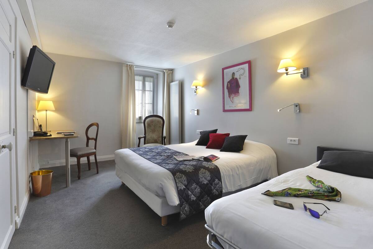 A hotel room with two beds, a desk, a chair, a TV, and a lamp.
