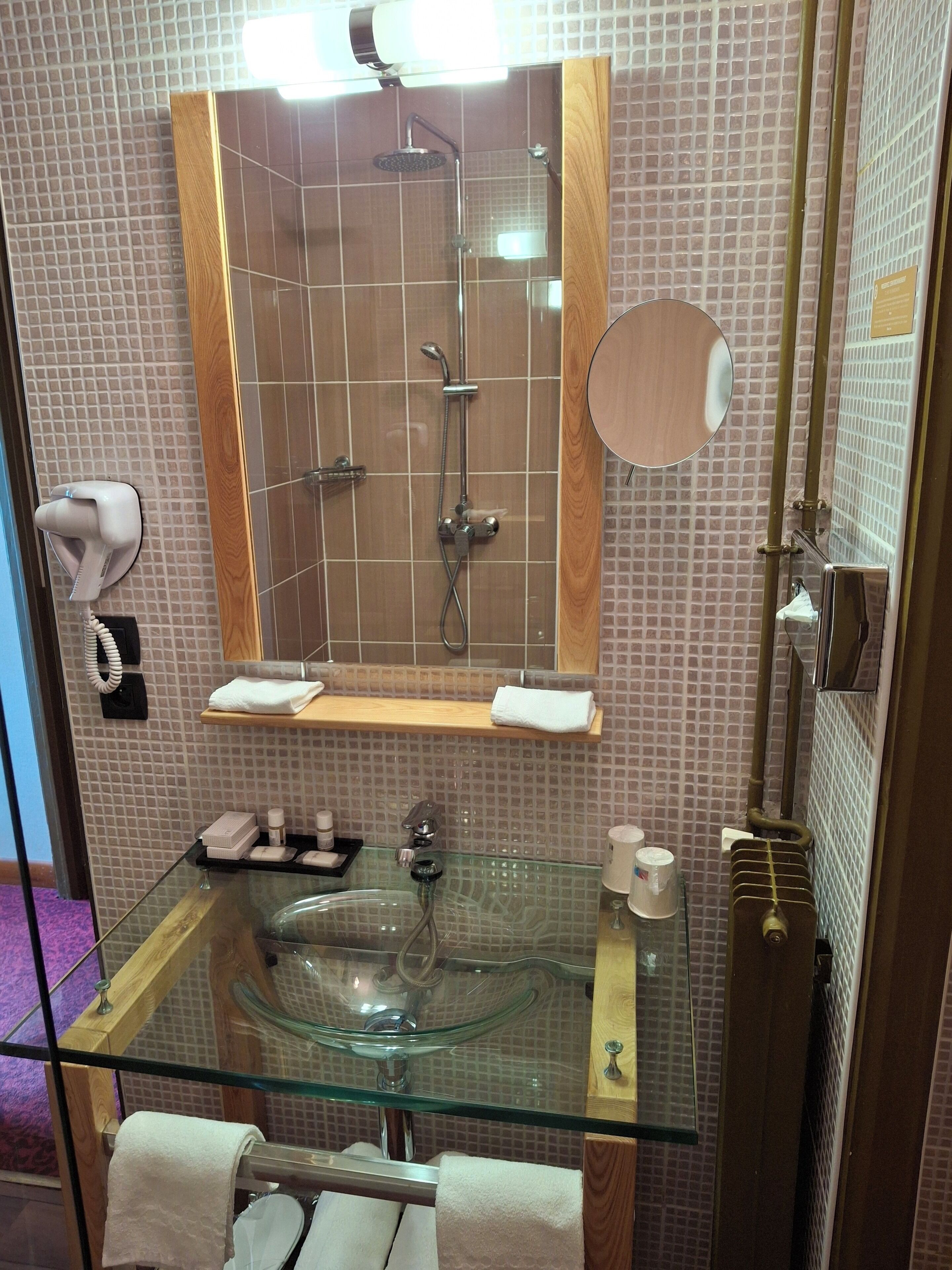 Een badkamer met een glazen wastafel, een spiegel, een douche en een handdoekrek.