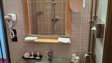 Een badkamer met een glazen wastafel, een spiegel, een douche en een handdoekrek.