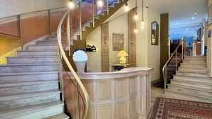 A grand staircase with a marble finish, leading to a reception area with a wooden counter and a lamp. - Hôtel La Tour Maje (Rodez)